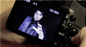 man in trench-coat reaches out from an LED camera screen